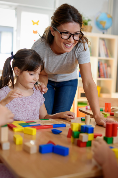 A child playing with blocks at a school near her teacher